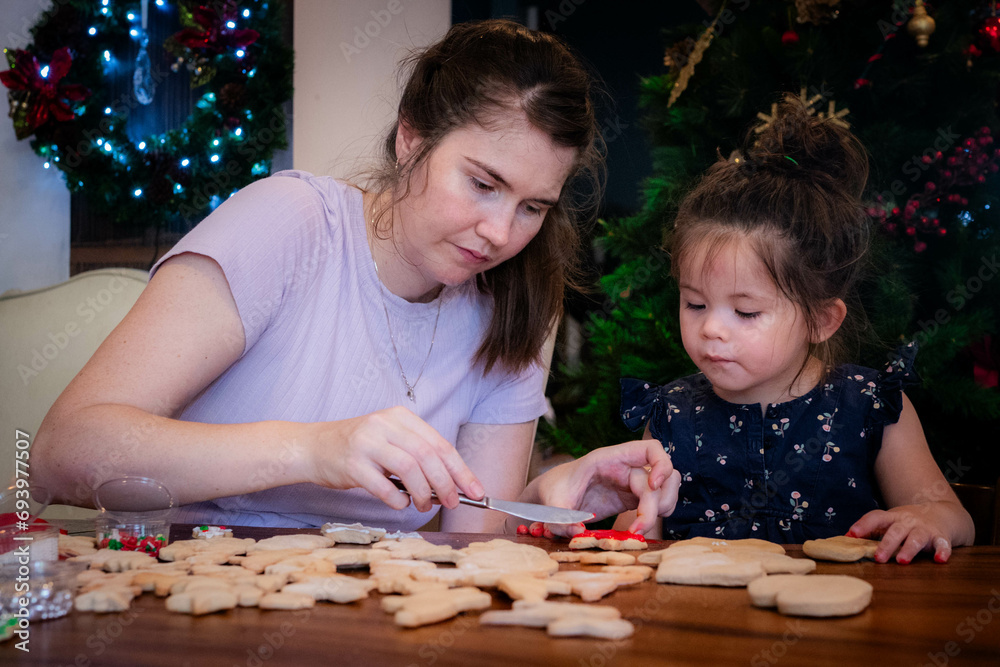 Mother and young daughter sit together and decorate Christmas cookies with icing Mother and young daughter sit together and decorate Christmas cookies with icing