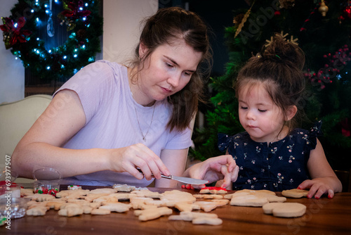 Mother and young daughter sit together and decorate Christmas cookies with icing
