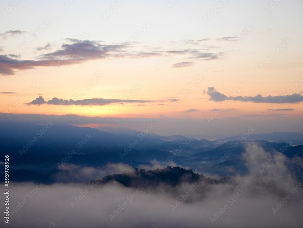 The mist flows through the mountain forest, Sun shining into tropical forest, Mist drifts through mountain ridges in the morning, slow floating fog blowing cover on the top of mountain