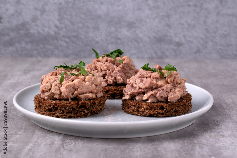 Canape with cod liver on brown bread served on the white plate on gray. Exquisite appetizer