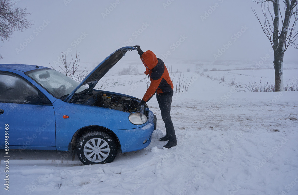 the car broke down in a blizzard in winter, car broke down on the road in winter, a man opens the hood to repair a car,the car does not start, the car stalls the car broke down in a blizzard in winter, car broke down on the road in winter, a man opens the hood to repair a car,the car does not start, the car stalls