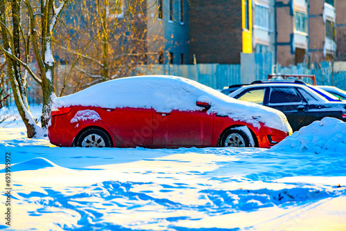Red car buried under snow after blizzard and snowfall in residential area.Snowdrifts and freezed vehicles.