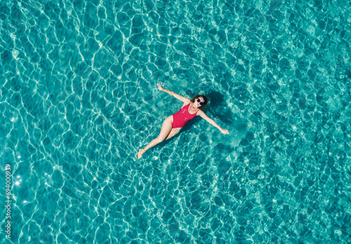 Top view of young pretty sexy girl in red swimsuit floating on water surface in crystal clear turquoise ocean. Happy island lifestyle.