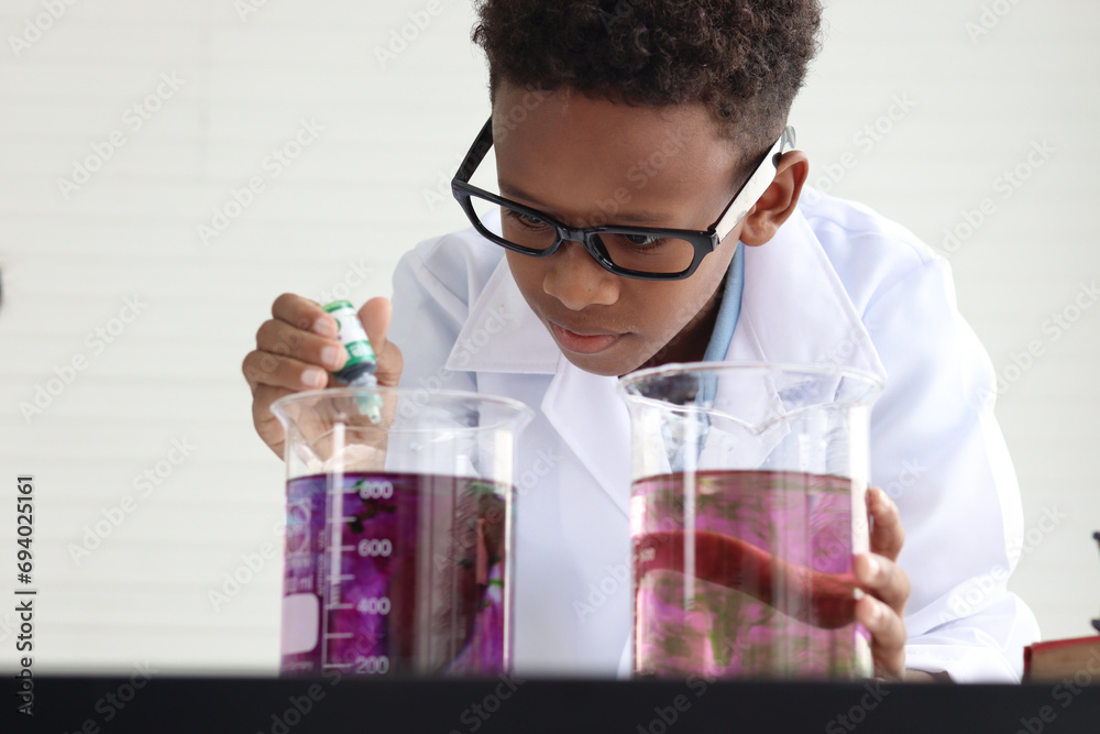 Concentrate African boy in lab coat holds chemical beaker for doing science experiment, young schoolboy kid scientist having fun in chemistry laboratory class, little child doing research at school. Concentrate African boy in lab coat holds chemical beaker for doing science experiment, young schoolboy kid scientist having fun in chemistry laboratory class, little child doing research at school.