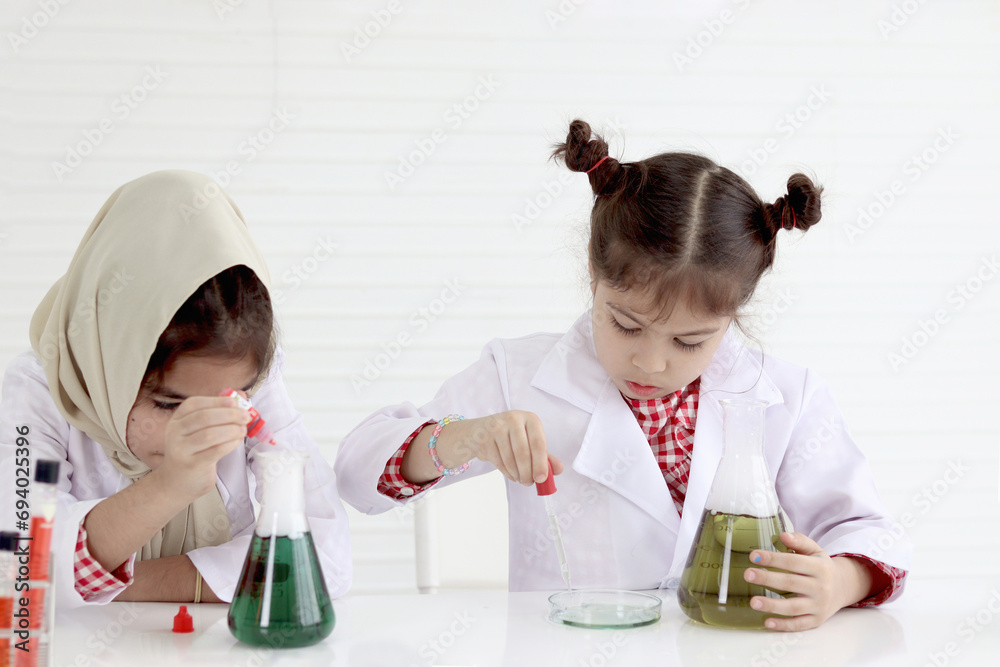 Cute little girl in lab coat doing science experiment together with her Muslim friend, young schoolgirl scientist kid having fun in chemistry laboratory class, little children doing research at school Cute little girl in lab coat doing science experiment together with her Muslim friend, young schoolgirl scientist kid having fun in chemistry laboratory class, little children doing research at school