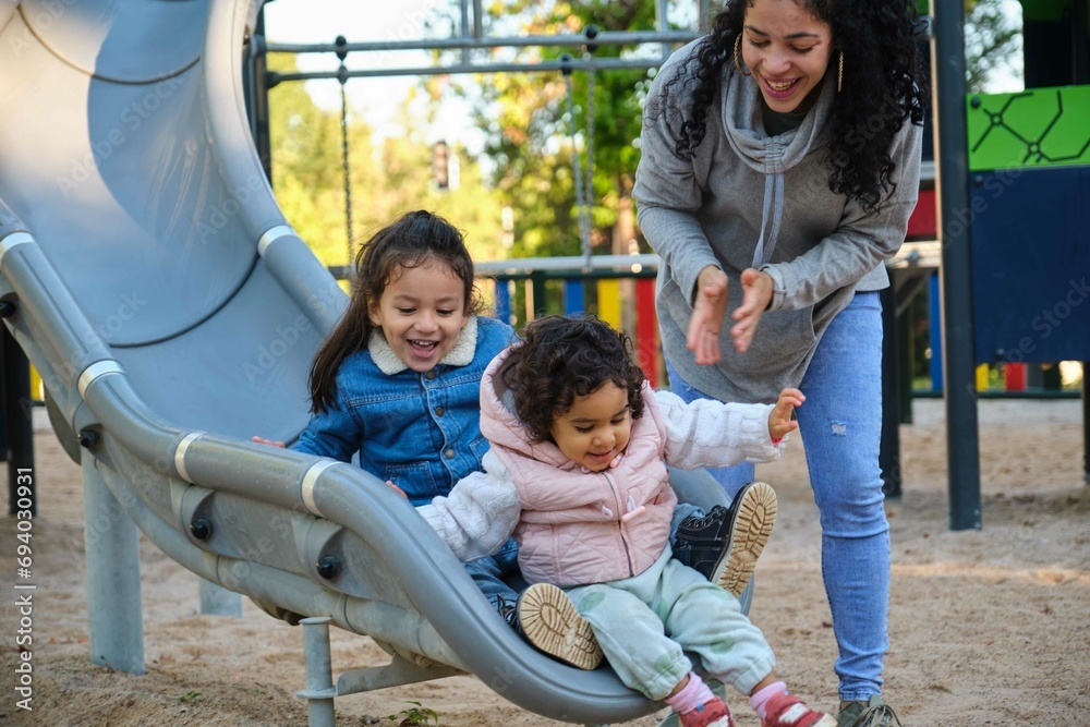 Happy Dominican mother playing with her children at the slide in a park. Latin family.