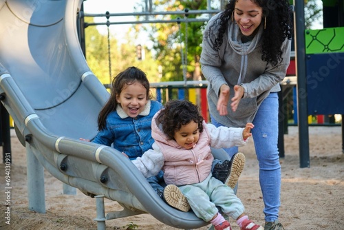 Happy Dominican mother playing with her children at the slide in a park. Latin family.