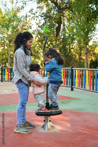 Картината върху платно Happy Dominican mother playing with her children at the synchro spinner in a park