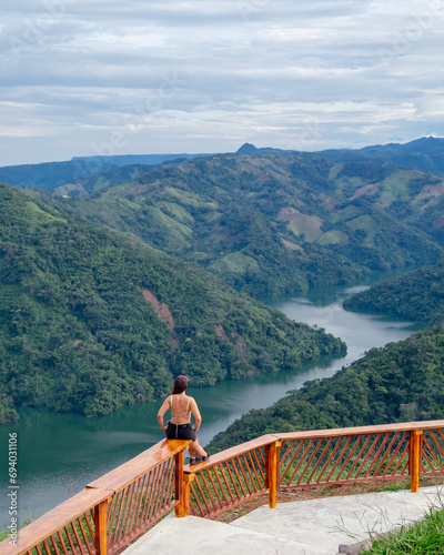 mujer sentada en un mirador viendo de fondo un rio entre montañas verdes en Colombia © Eduard
