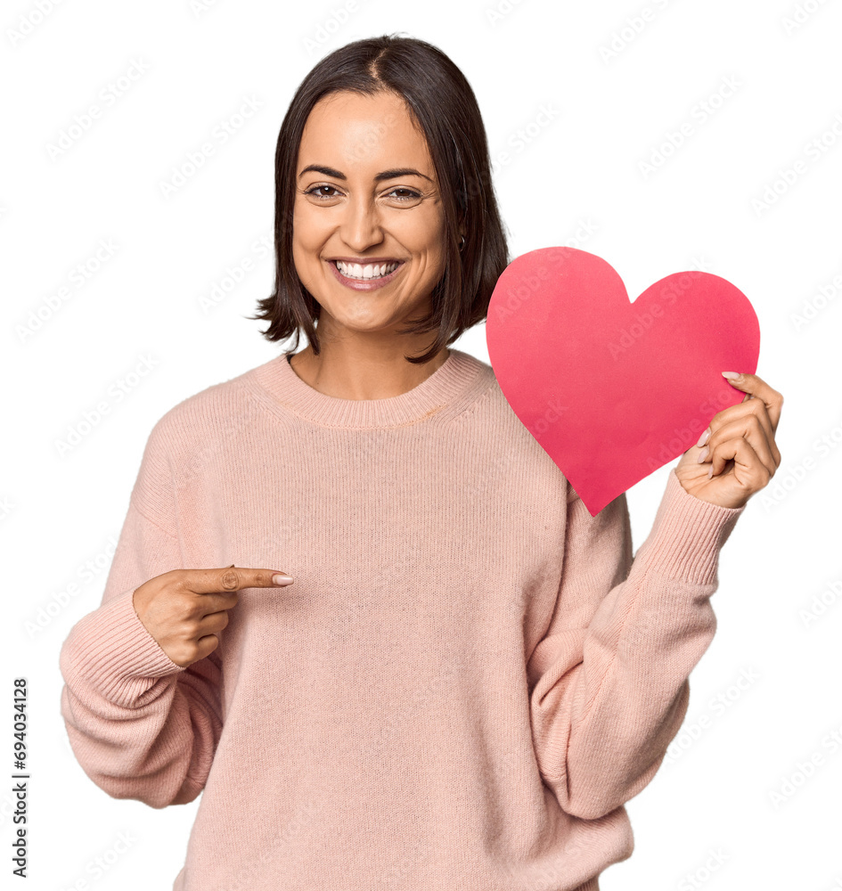 Young woman holding Valentine's heart smiling and pointing aside, showing something at blank space. Young woman holding Valentine's heart smiling and pointing aside, showing something at blank space.