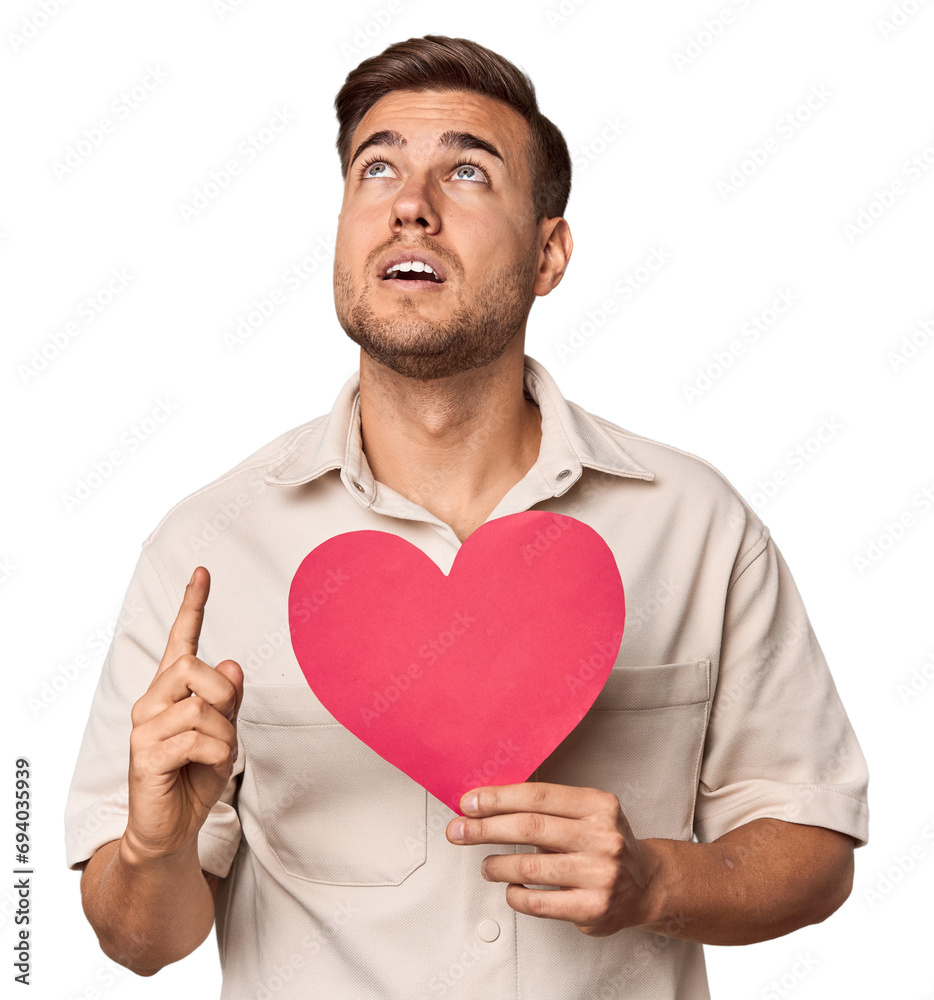 Young man holding a heart pointing upside with opened mouth. Young man holding a heart pointing upside with opened mouth.
