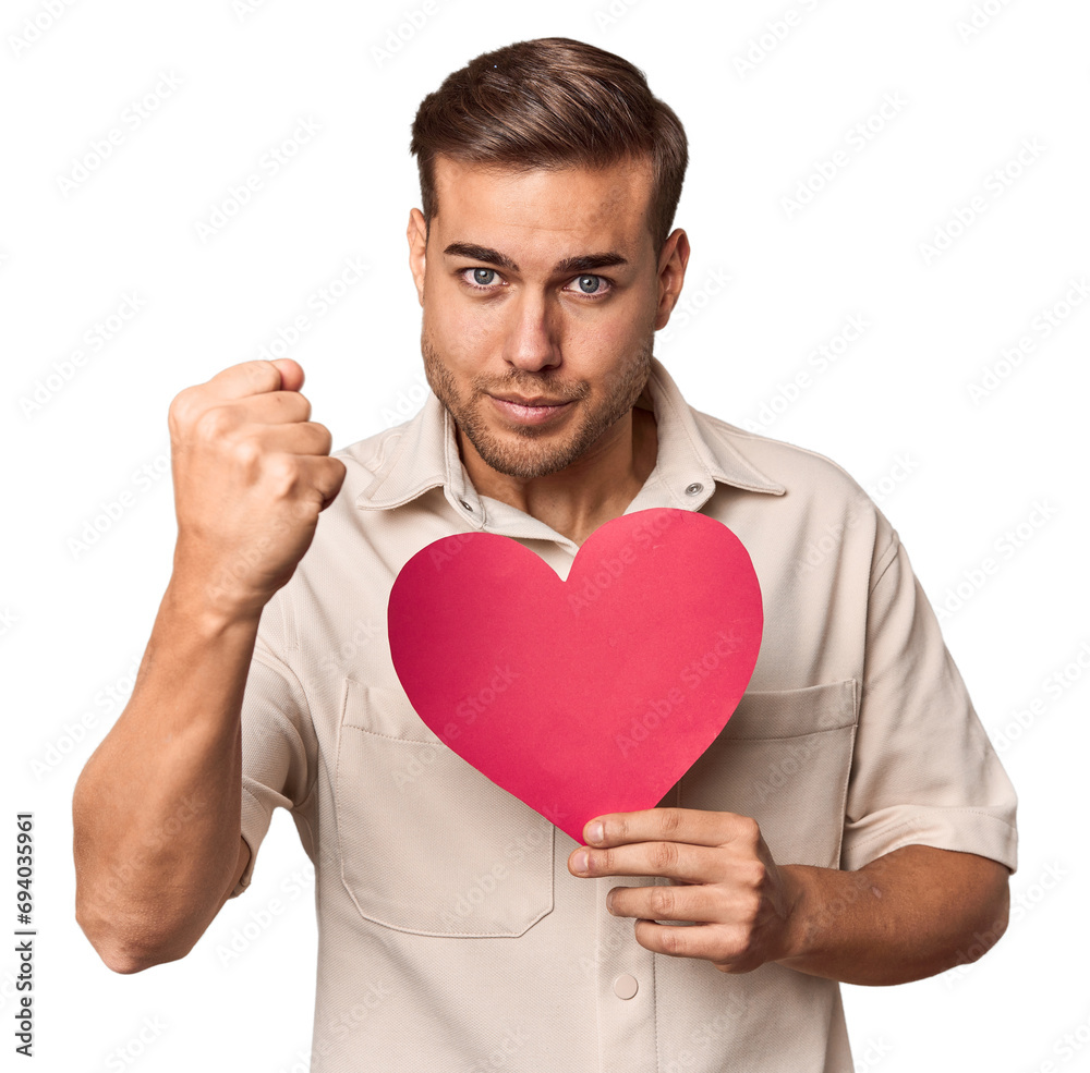 Young man holding a heart showing fist to camera, aggressive facial expression. Young man holding a heart showing fist to camera, aggressive facial expression.