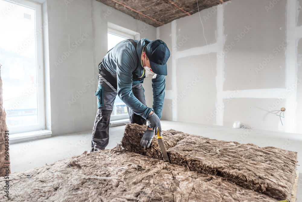 Ceiling insulation. Cutting a thermal insulation from glass wool using a knife for stone wool. iling thermal insulation. - obrazy, fototapety, plakaty 