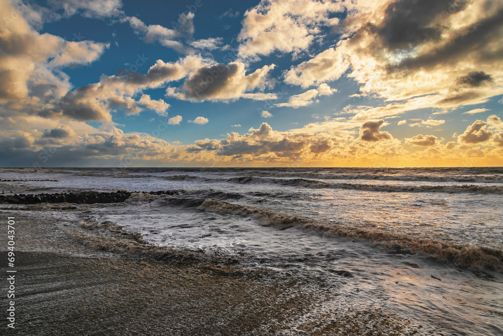 Big waves crash on the shore under a cloudy sky. An impressive sky with luminous clouds. An epic seascape. Colorful glowing golden clouds during a storm. The Black Sea during a storm. 