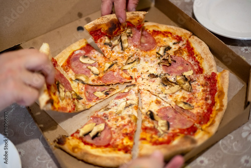 large pizza on the table in a box, cut into pieces, which people take with their hands at the feast.