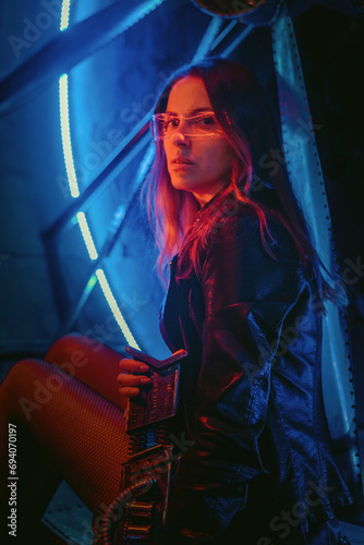Beautiful girl in the leather jacket and short dress posing in the neon lights background.