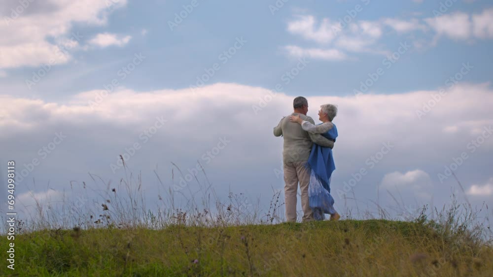 Senior couple dancing a waltz on a hill against a sky with clouds. Concept of happy family life. Senior couple dancing a waltz on a hill against a sky with clouds. Concept of happy family life.