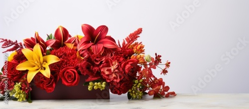 Professional florist creates a red floral arrangement in a red box, featuring orchids, roses, sunflowers, lilies, alstroemerias, and ornithogalums, displayed on a white brick wall. photo