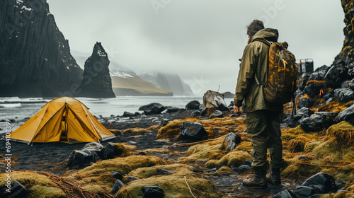 Solitary hiker beside a yellow tent in a rugged Icelandic landscape, with overcast skies and basalt cliffs.