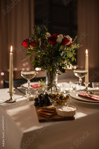 holidays, romantic date and celebration concept - close up of festive table serving for two with flowers in vase and candles burning at home on valentine's day