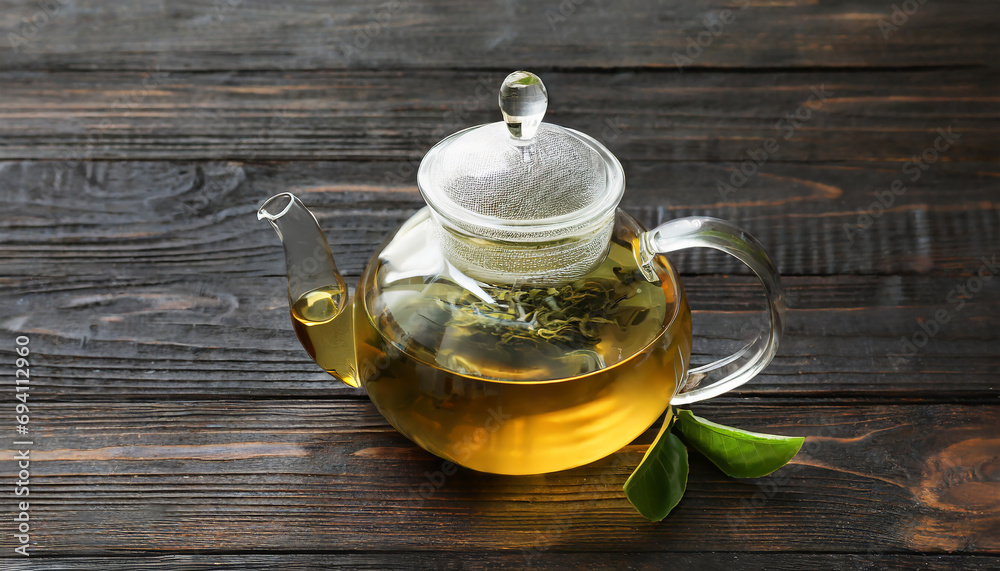 Glass teapot with green tea on dark wooden background Glass teapot with green tea on dark wooden background