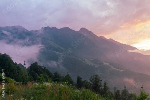 Fog and clouds in the mountains against the backdrop of the setting sun, changeable weather in the mountains, clouds and nebula on mountain peaks wide