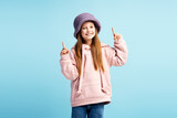Portrait of smiling cute girl wearing hat, stylish casual clothes pointing fingers on copy space looking at camera isolated on blue background. shopping, store, advertisement concept