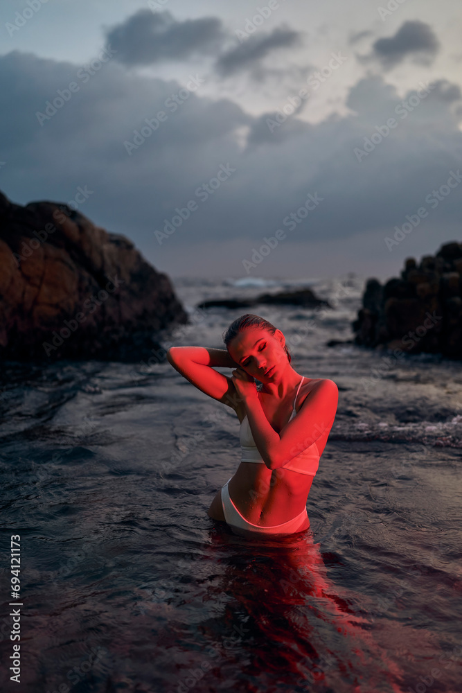 Attractive woman enjoys serene night swim in ocean bathed in red light, embodying tranquil travel and self-care moments at sea.