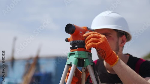 Close up shot of professional Construction Worker Using Theodolite Surveying Optical Instrument. Man wearing hard hat and work gloves measures angles for building plans. photo