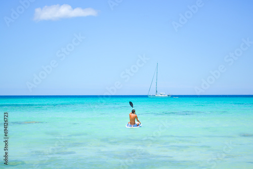 
A beautiful view of a person paddle boarding and a yacht in azure blue Caribbean Sea. 
