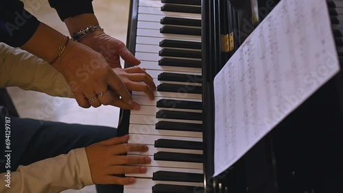 View from above of hands of a musician teacher and boy fingers touching the piano keys, explaining the true positions of fingers while learning play piano and capturing the rhythm of music