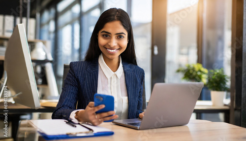 Smiling businesswoman working at office using laptop and smartphone for 2FA