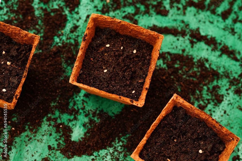 Top view of three square biodegradable pots filled with dark, moist soil. Small, visible seeds of tomato are planted in soil, ready for germination. Eco-friendly planting, beginning of growing season Top view of three square biodegradable pots filled with dark, moist soil. Small, visible seeds of tomato are planted in soil, ready for germination. Eco-friendly planting, beginning of growing season
