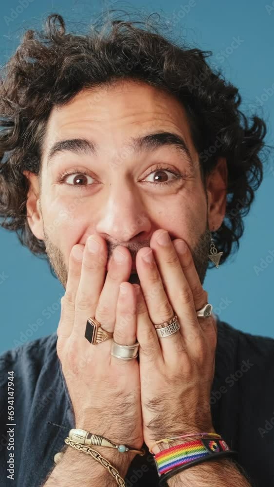 Close up, surprised man covers his mouth with palms looking at camera isolated on blue background Close up, surprised man covers his mouth with palms looking at camera isolated on blue background