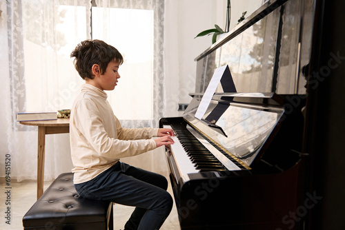 Talented teenage boy pianist musician creates music and song, performs on the pianoforte, composes a melody.
