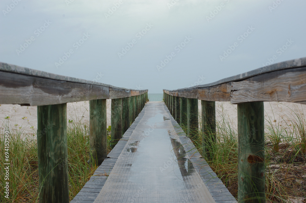 Fototapeta premium Mid level view out leading lines of Treasure Island Florida beach access bridge with reflections of water . Green grass beach and sand out the sides with water in distance. 