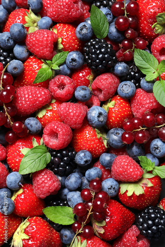 Assortment of fresh ripe berries with green leaves as background, top view