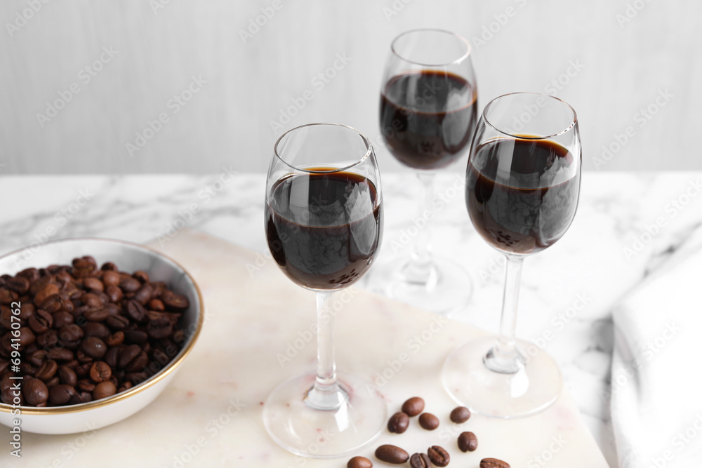 Glasses of coffee liqueur and beans on white table