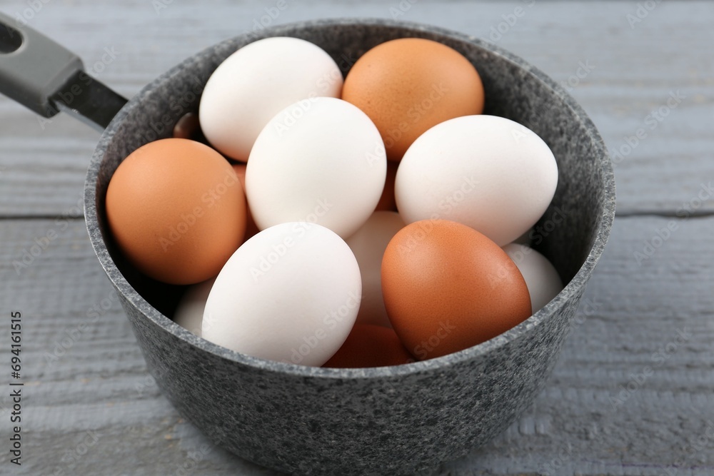 Unpeeled boiled eggs in saucepan on grey wooden table, closeup Unpeeled boiled eggs in saucepan on grey wooden table, closeup