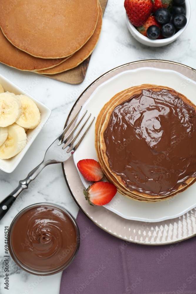 Tasty pancakes with chocolate paste, berries and fork on white marble table, flat lay Tasty pancakes with chocolate paste, berries and fork on white marble table, flat lay
