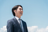 青空の中にいる笑顔の若いアジア人ビジネスマン（転職・成功・未来・チャレンジ・希望・目標・達成）
