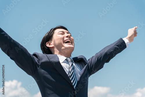 青空の中で叫ぶ若いアジア人ビジネスマン（転職・勝利・就職・脱サラ・チャレンジ・頑張る・達成）
 photo