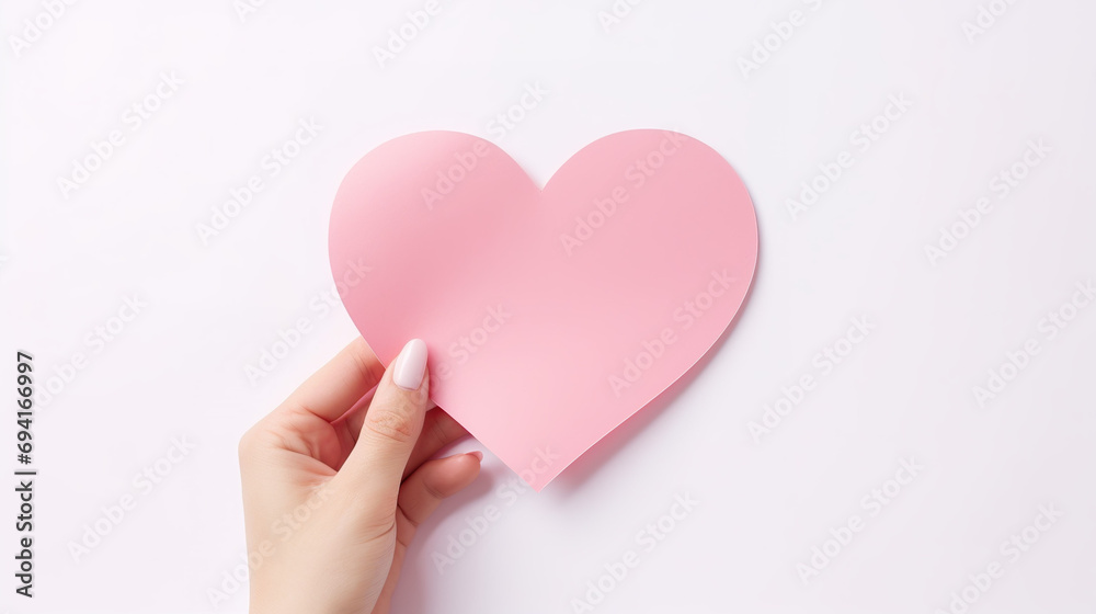 Hand holding heart-shaped pink paper on white background. 