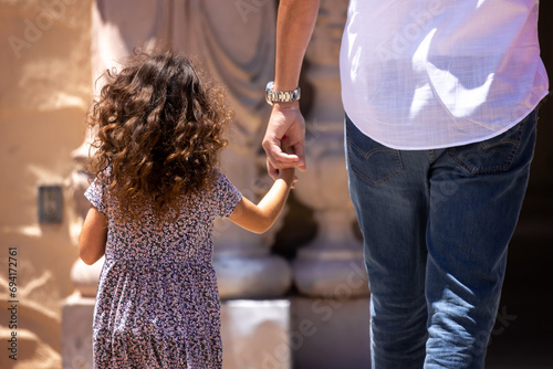 Child holding parents hand while walking outside.
