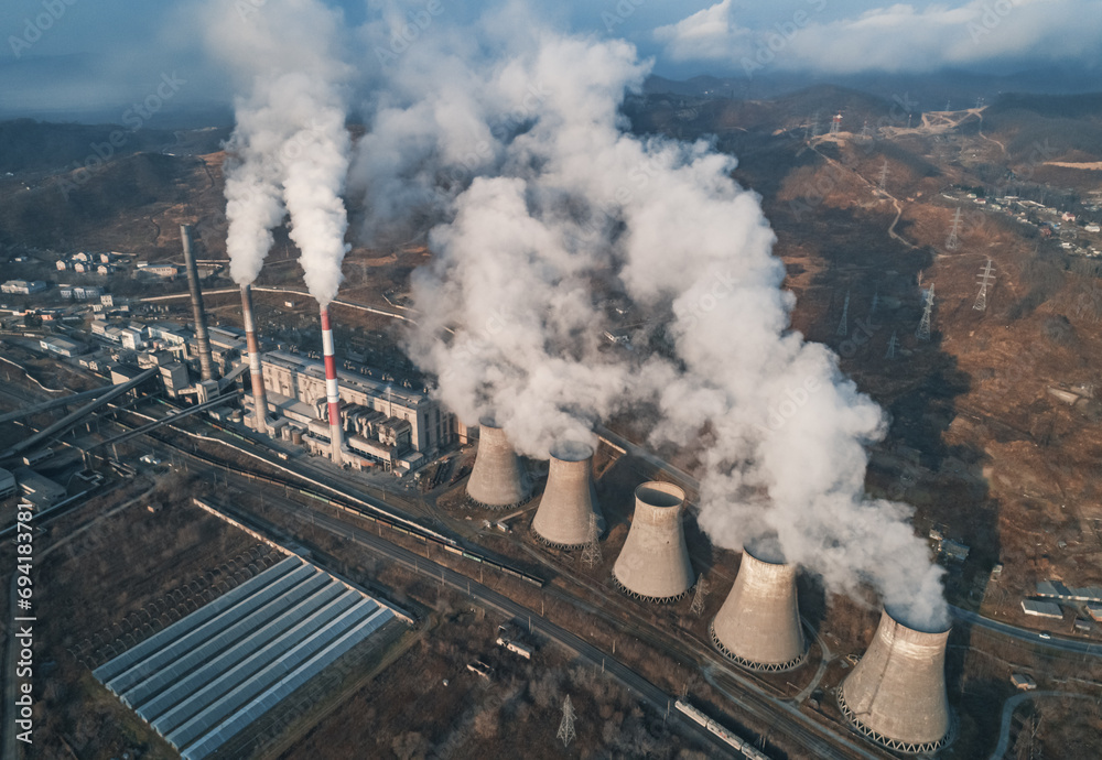 Aerial view of tall chimney pipes with grey smoke from coal power plant. Production of electricity with fossil fuel. Ecology and pollution of nature.