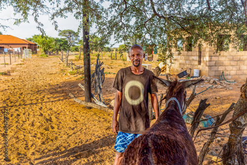 african man in the village, standing in the yard with a donkey