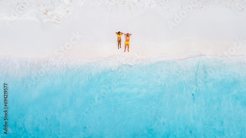 Drone top view of a couple of men and women lying down on the beach of Small Curacao Island, a couple relaxing on the beach of Curacao, top view at a tropical beach photo