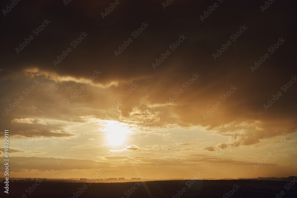 Obraz premium Dark storm clouds and sun over the houses of the evening city