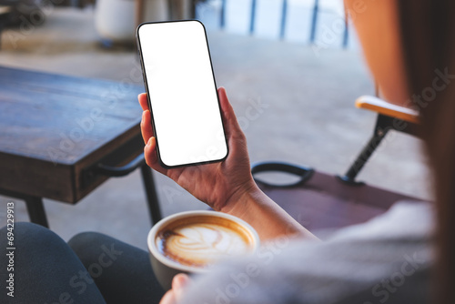 Mockup image of a woman holding mobile phone with blank desktop screen while drinking coffee in cafe photo