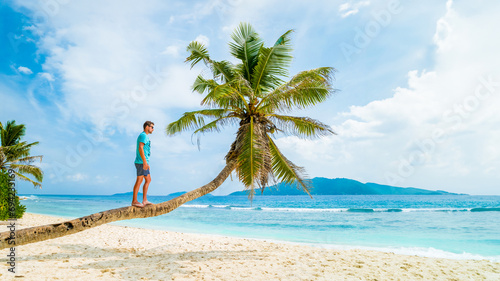 Young men relaxing at a palm tree on a tropical white beach at the La Digue Seychelles Islands.